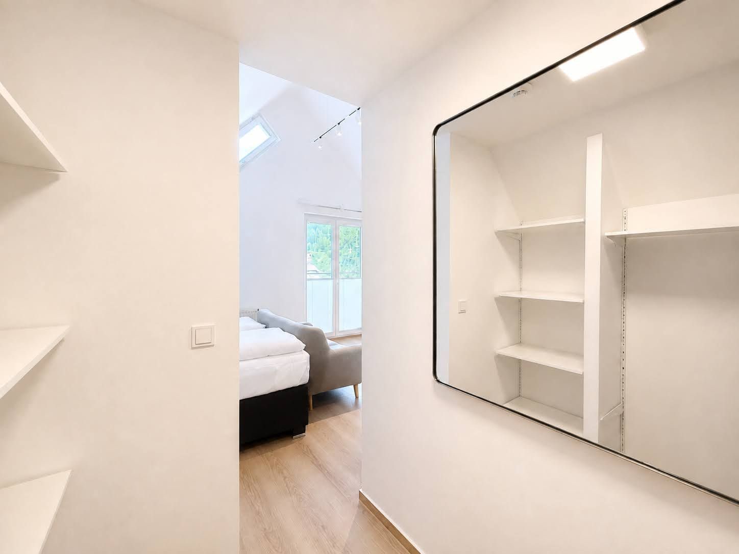 Quarto moderno e minimalista com um espelho grande, uma cama e vista para o exterior.