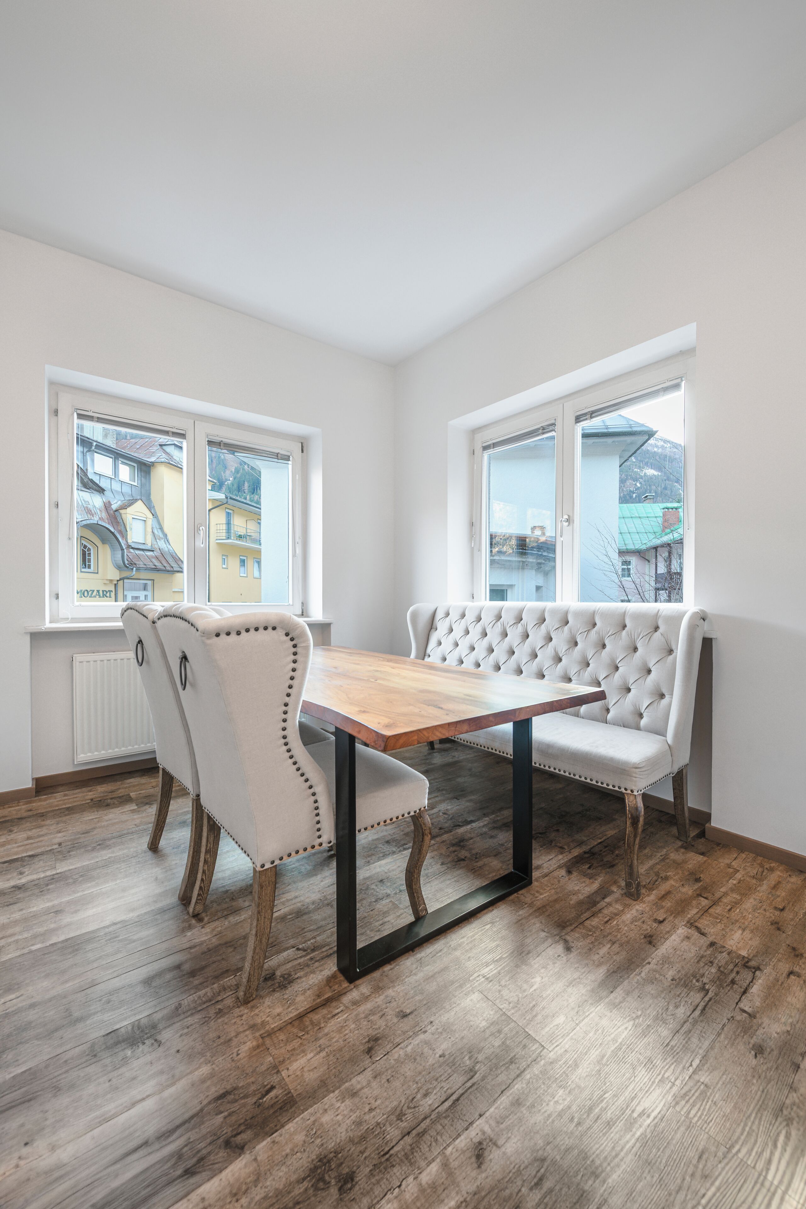 Un espace repas avec une table en bois et deux bancs blancs recouverts de tissu.