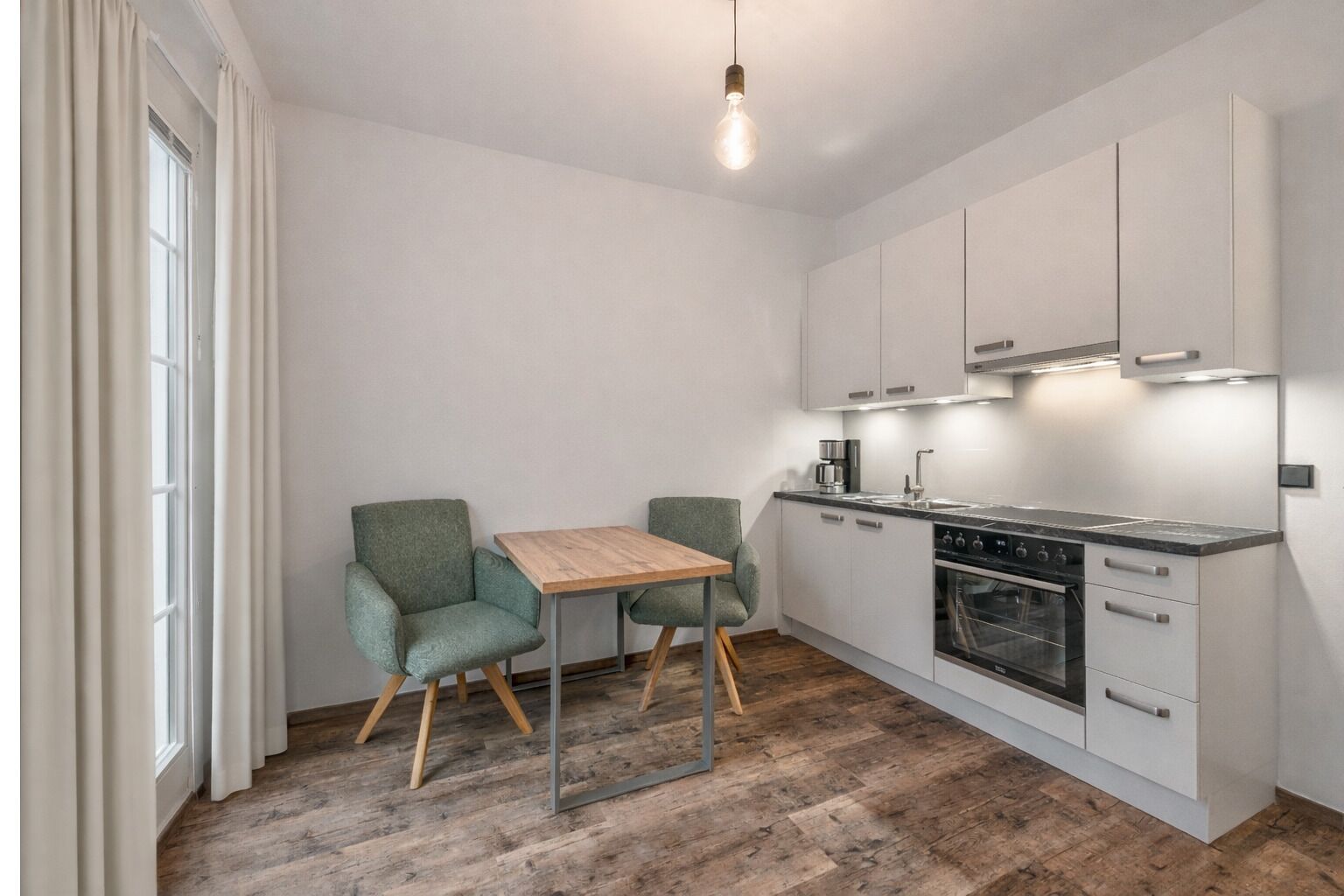 Una cocina compacta con una mesa de comedor y dos sillas, horno empotrado y cafetera.