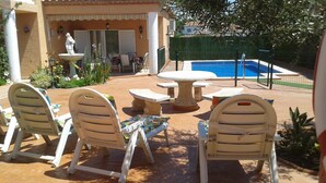 Un patio al aire libre con sillas de plástico blanco y una mesa, una pequeña fuente y una piscina.