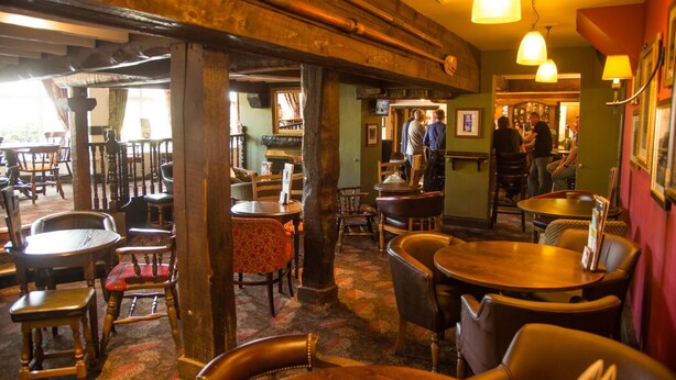 Un restaurant chaleureux avec des poutres en bois, des tables rondes et des chaises.