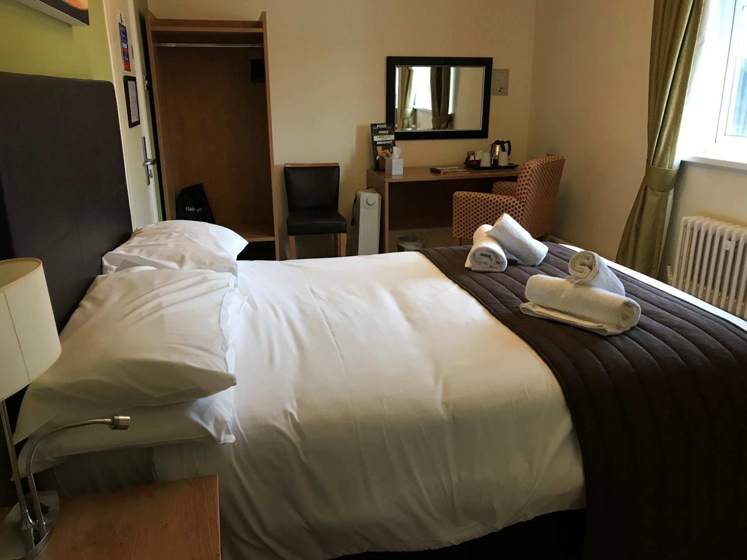 A hotel room with a bed, a desk, a chair, a mirror, and a window with curtains.