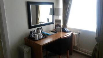 A hotel room with a desk, a mirror, a lamp, a telephone, and a radiator.