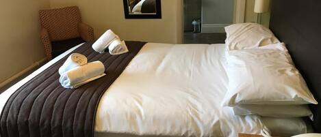 Habitación de hotel con cama, una silla, mesita de noche con teléfono y espejo que refleja el baño.