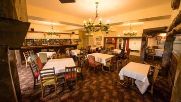 A restaurant with multiple tables and chairs, a bar area, and a chandelier.