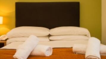 A neatly made bed with white linens and rolled towels, a dark headboard, and a bedside lamp.