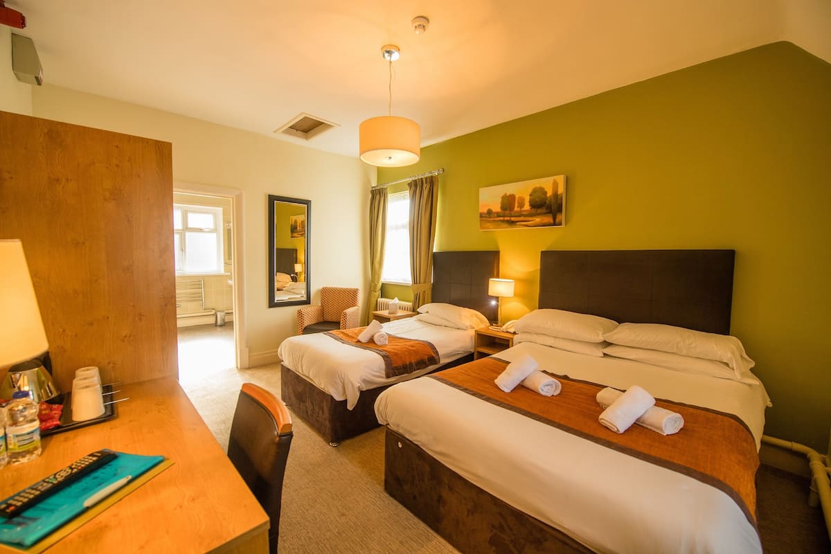 Habitación de hotel con dos camas, un escritorio con lámpara, una silla y un cuadro en la pared.