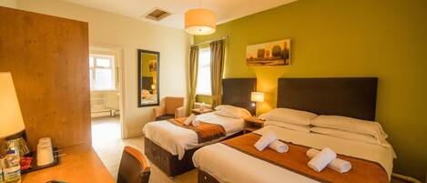 A hotel room with two beds, a desk with a lamp, a chair, and a painting on the wall.