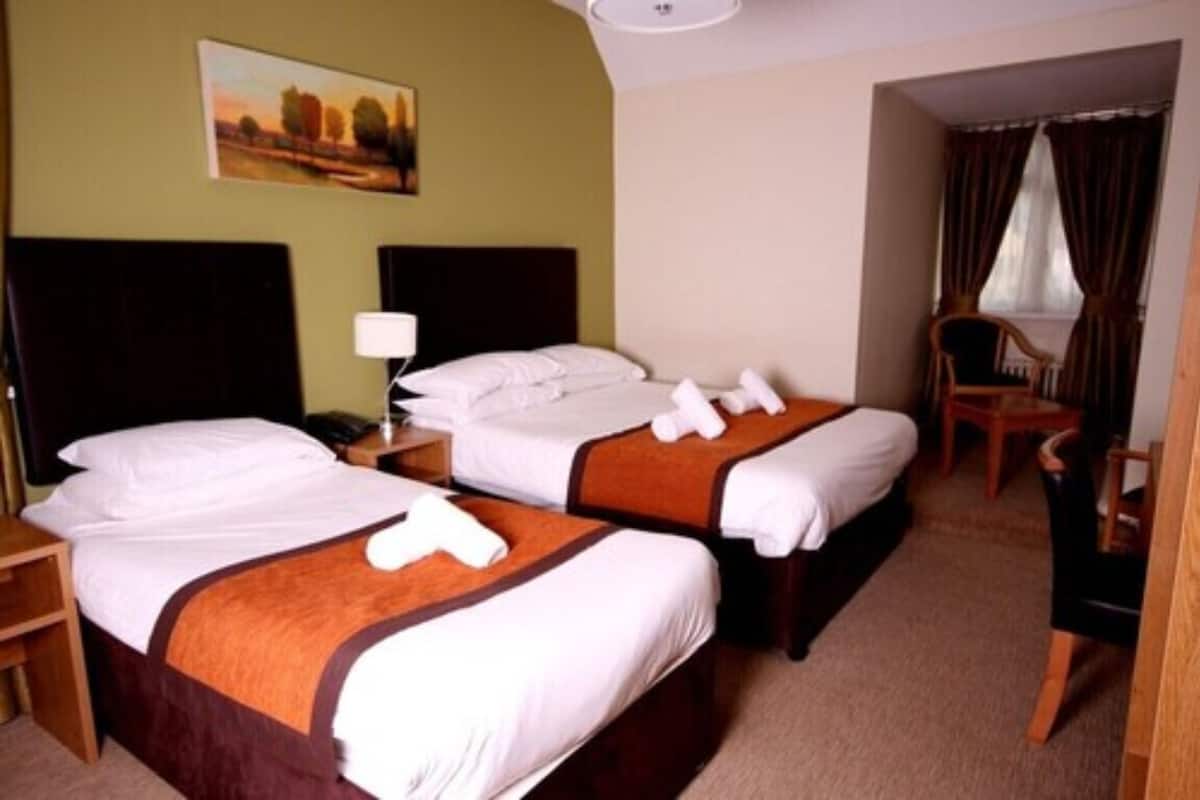 Una habitación de hotel con dos camas, una mesita de noche, una silla y un cuadro en la pared.