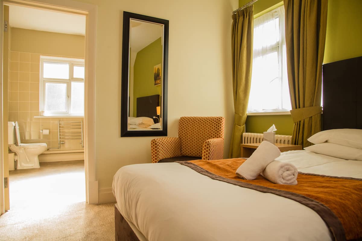 Una habitación de hotel con cama, una silla, un espejo y una ventana con cortinas.