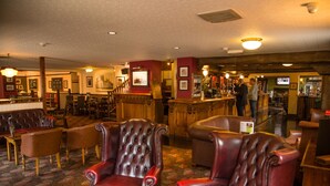 Un hall d’entrée avec des fauteuils en cuir, des tables en bois et un coin bar.