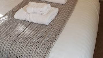 A neatly made bed with white linens and a striped blanket, a wooden wardrobe, and a mirror on the wall.