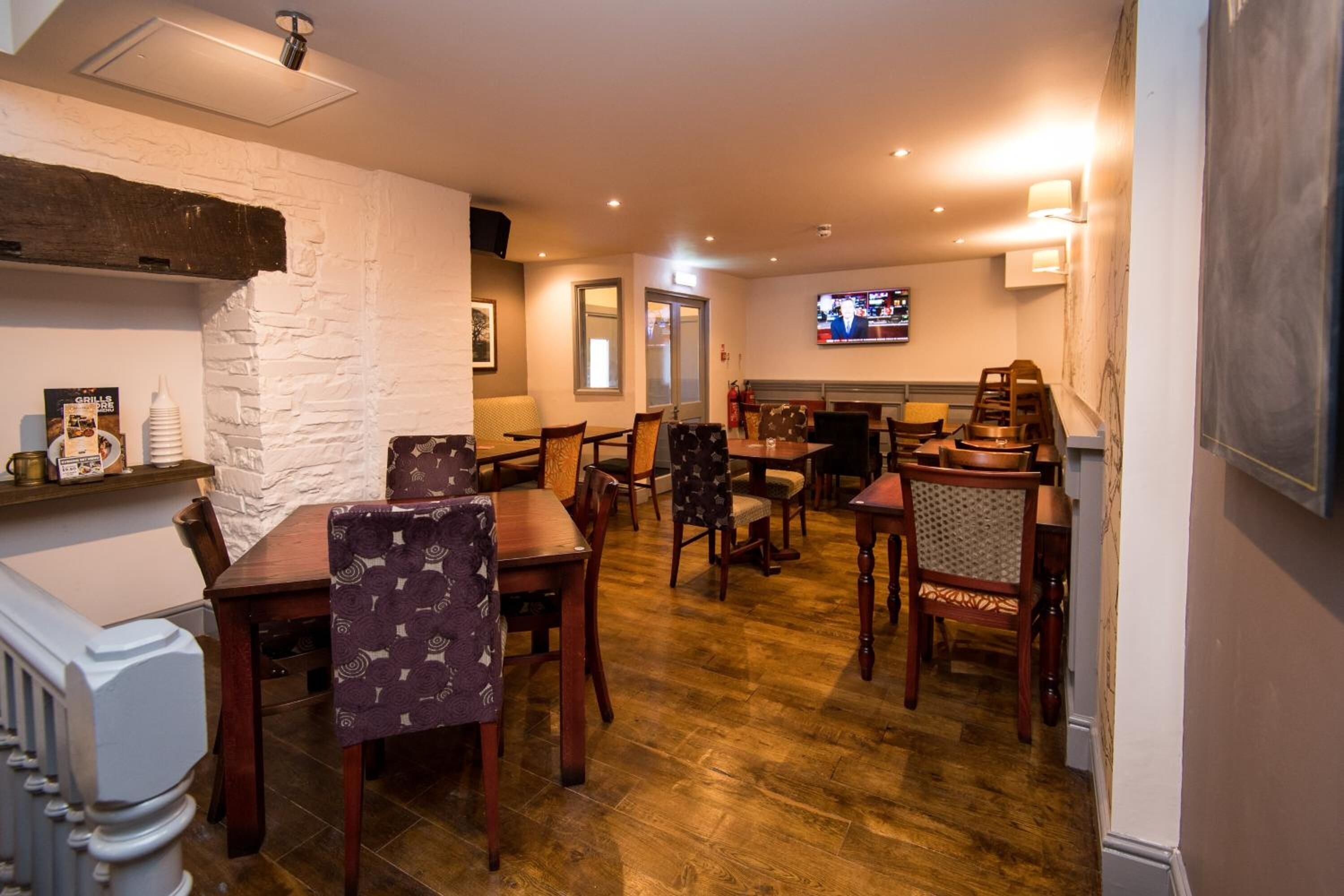A restaurant with wooden flooring, white brick walls, and multiple dining tables and chairs.