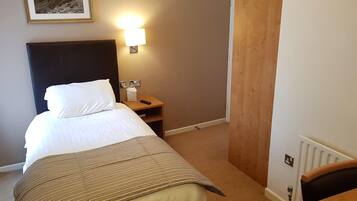 A hotel room with a bed, a bedside table with a lamp, a wooden wardrobe, and a framed picture on the wall.