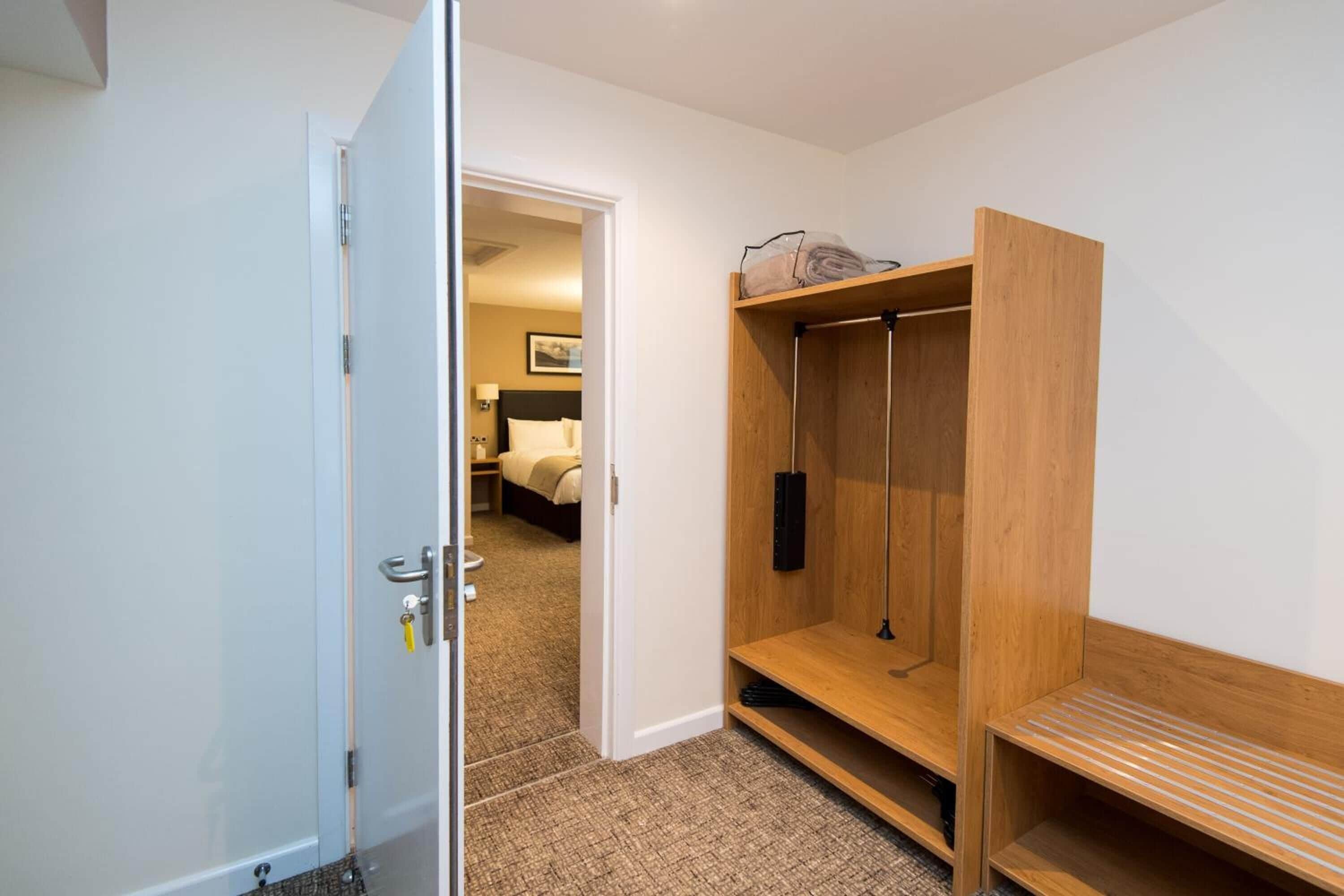A hotel room with a wooden wardrobe, a bed, and a bathroom visible through an open door.