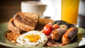 Un plato con tostadas, huevos, salchichas, tomates, frijoles y un vaso de jugo de naranja.