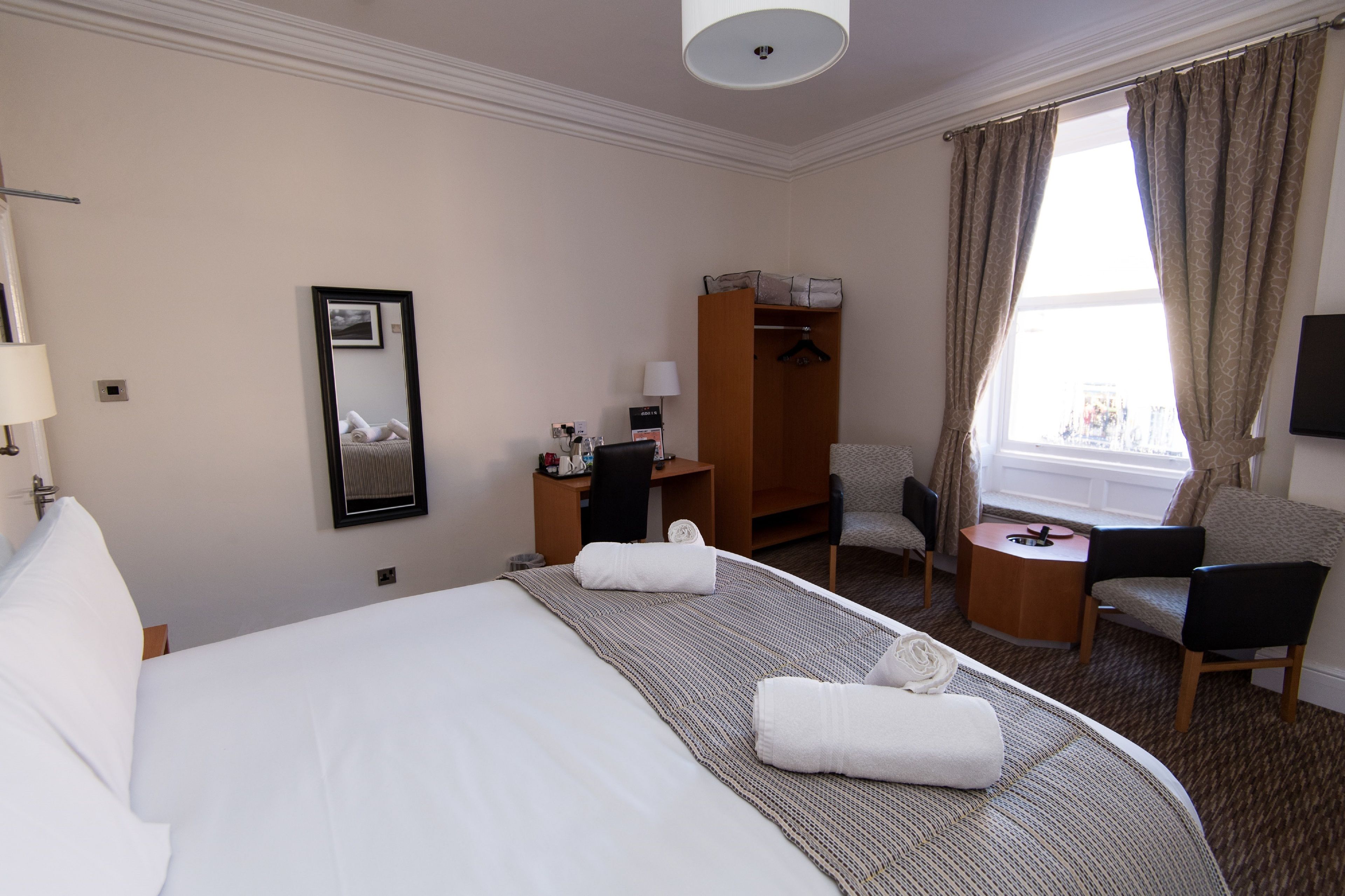 Een hotelkamer met een groot bed, een bureau, een stoel, een kleine tafel, een kledingkast en een televisie.