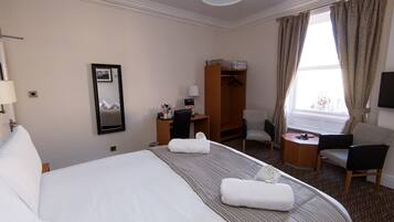Een hotelkamer met een groot bed, een bureau, een stoel, een kleine tafel, een kledingkast en een televisie.