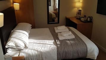 A hotel room with a neatly made bed, two bedside lamps, a bedside table with a lamp, a mirror, and a flat-screen TV.