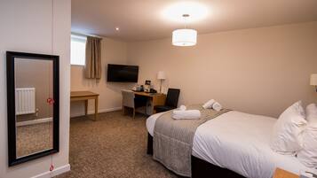 A hotel room with a bed, a desk, a chair, a television, and a mirror.