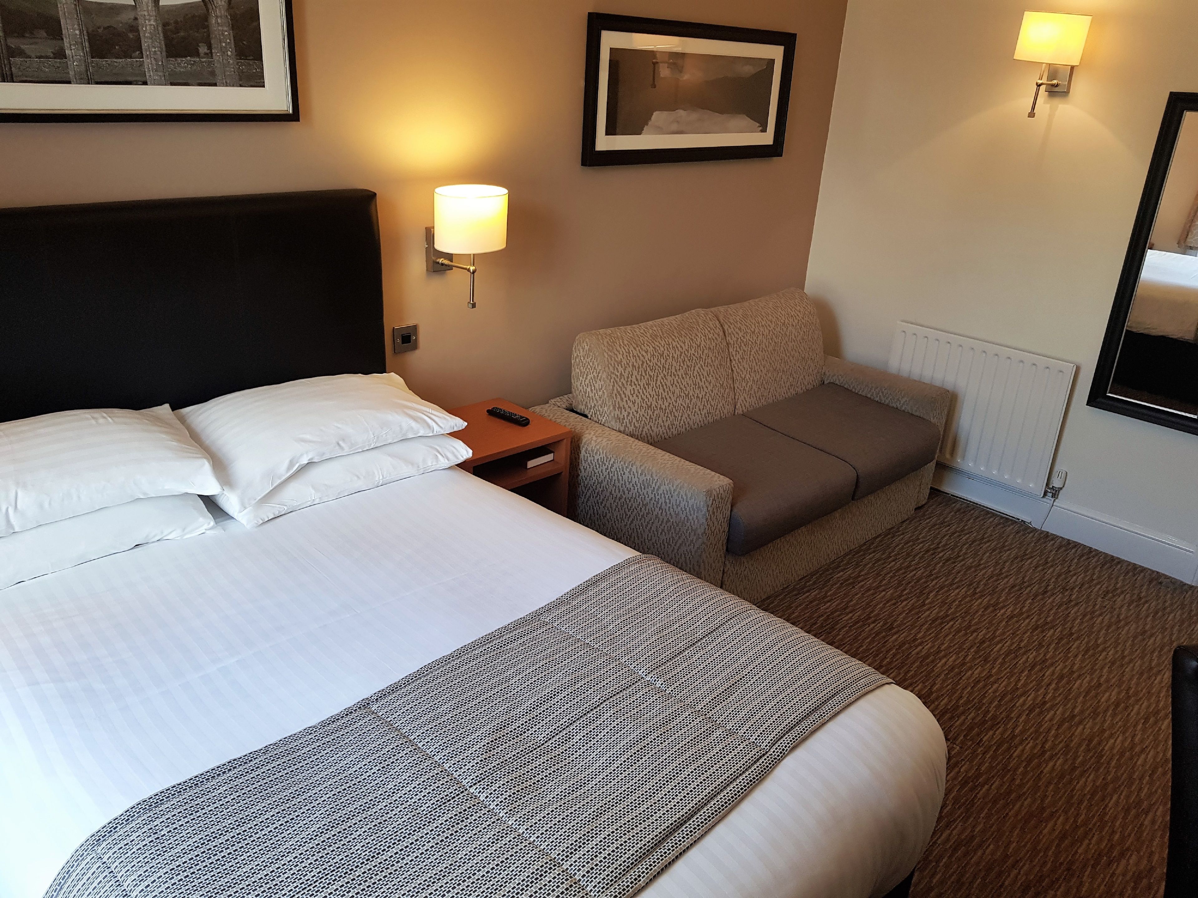 Ein Hotelzimmer mit einem großen Bett, einer Couch, einem Nachttisch mit Lampe und einem gerahmten Bild an der Wand.