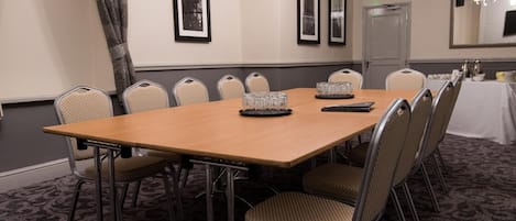 Un salón de conferencias con una larga mesa, sillas, cuadros en la pared y una puerta al fondo.