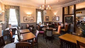 A restaurant with wooden tables and chairs, framed pictures on the walls, and a chandelier.
