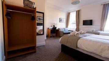 A hotel room with a large wardrobe, a desk with a chair, two beds with towels, a television, and a window with curtains.