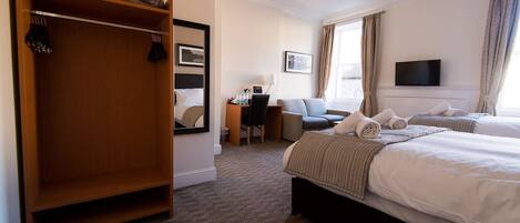 A hotel room with a large wardrobe, a desk with a chair, two beds with towels, a television, and a window with curtains.