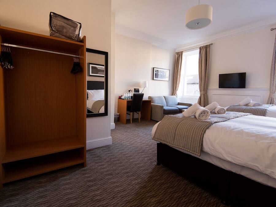 A hotel room with a large wardrobe, a desk with a chair, two beds with towels, a television, and a window with curtains.