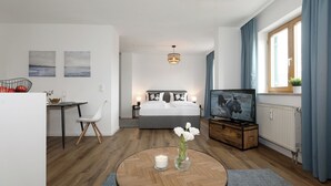 A modern hotel room with a bed, TV, desk, chair, and a view of the city. - Hotel Obermaier (Munich)