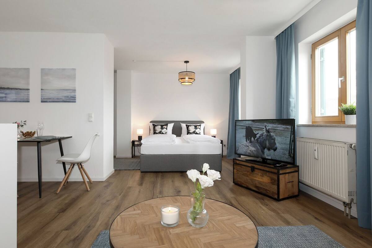 A modern hotel room with a bed, TV, desk, chair, and a view of the city.