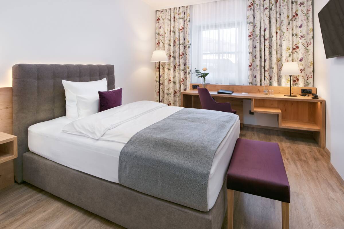 A modern hotel room with a large bed, a desk, and a chair.