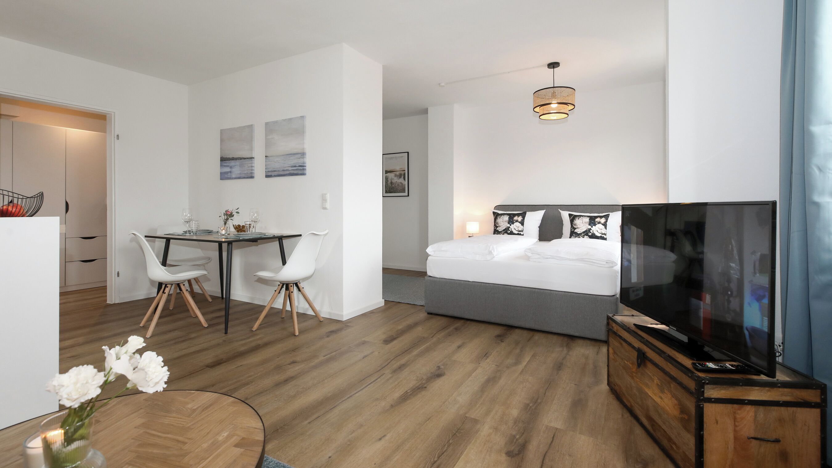 Una habitación de hotel con cama, televisión, zona de comedor con sillas y mesa, y un pasillo.
