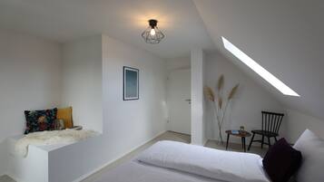 A modern bedroom with a loft-style ceiling, a bed, a small seating area, and a skylight.