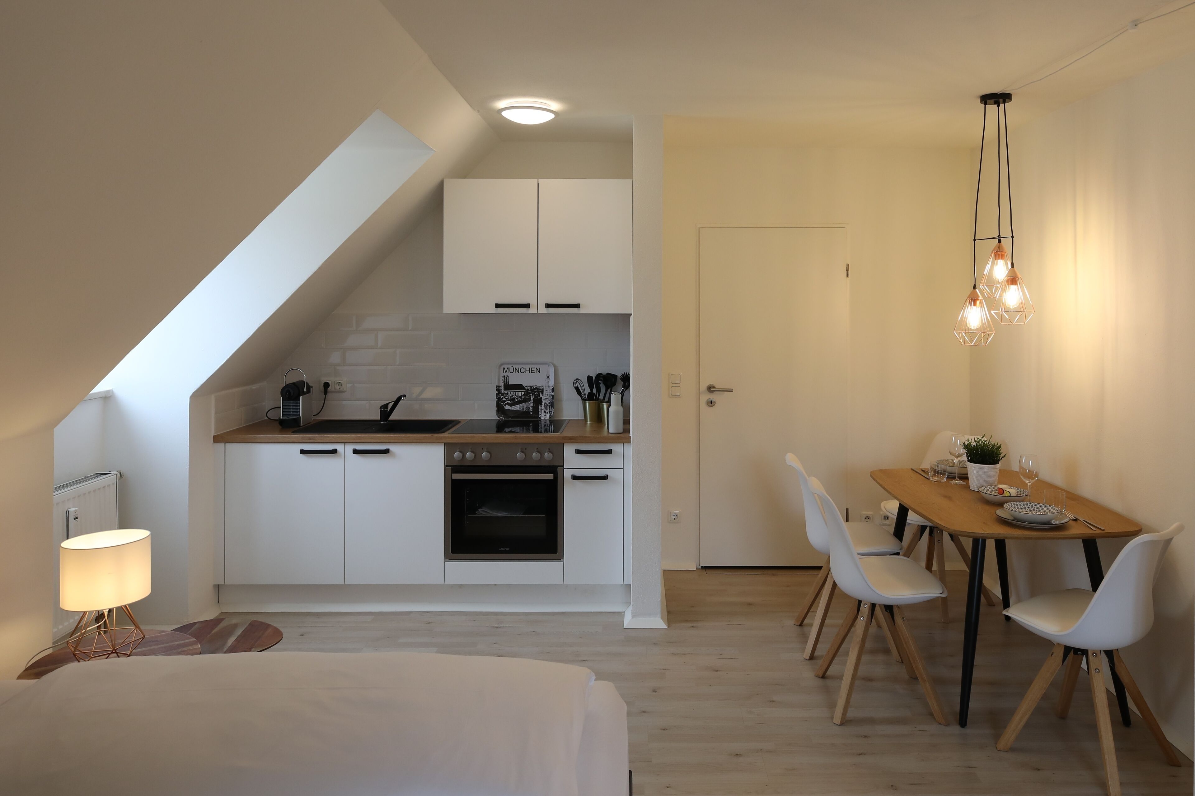 Une cuisine moderne avec des meubles blancs, un coin repas doté d’une table et de chaises en bois, et un luminaire au plafond.