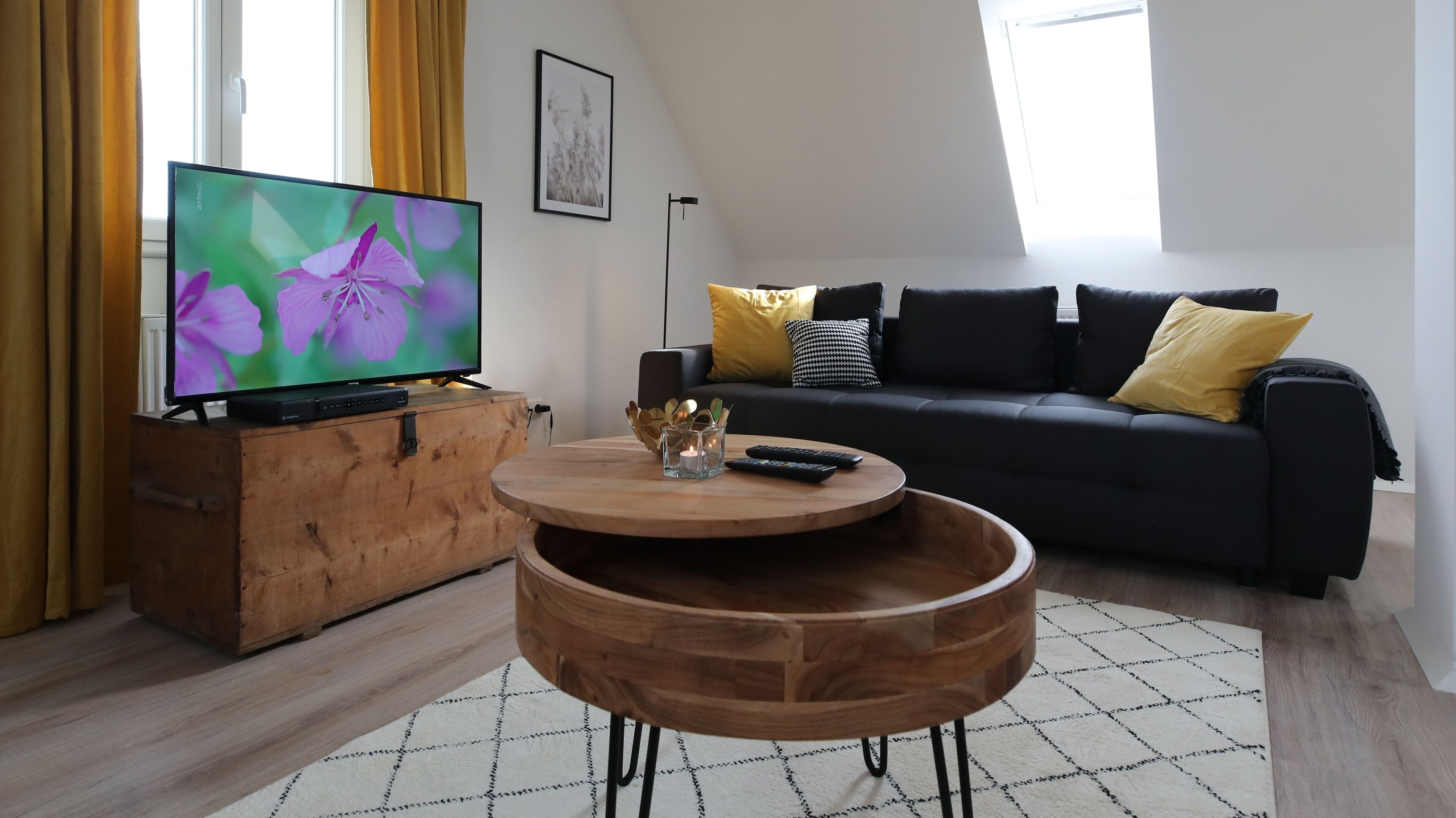 Una sala de estar moderna con un televisor de pantalla plana, una mesa de centro de madera, un sofá negro y una alfombra estampada.