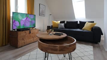 Una sala de estar moderna con un televisor de pantalla plana, una mesa de centro de madera, un sofá negro y una alfombra estampada.