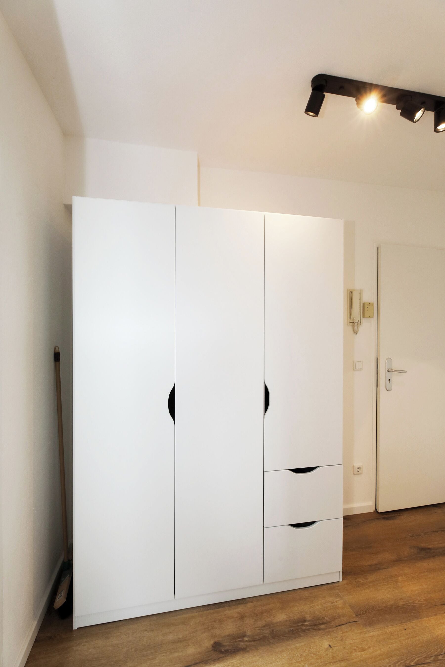 A room with a white wardrobe, a door with a handle, and a light fixture on the ceiling.