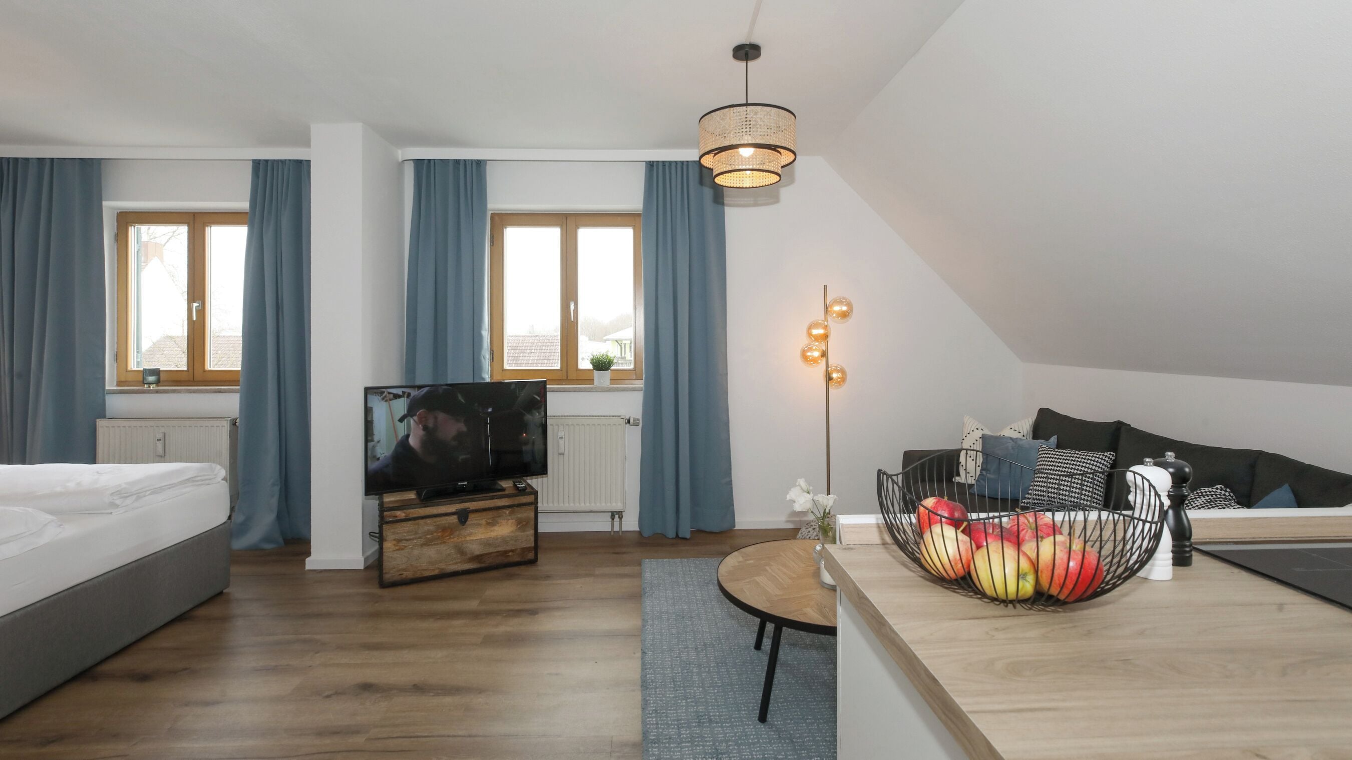 Una habitación de hotel moderna con cama, televisor, cómoda de madera y un área de comedor con frutero.