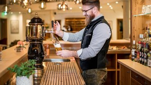 A bartender pouring beer into a glass at a bar with a modern design, including pendant lights and a variety of bottles on shelves. - Hotel Obermaier (Munich)