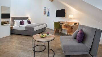 A modern, well-lit room with a bed, a sofa, a desk, and a round table with fruit.