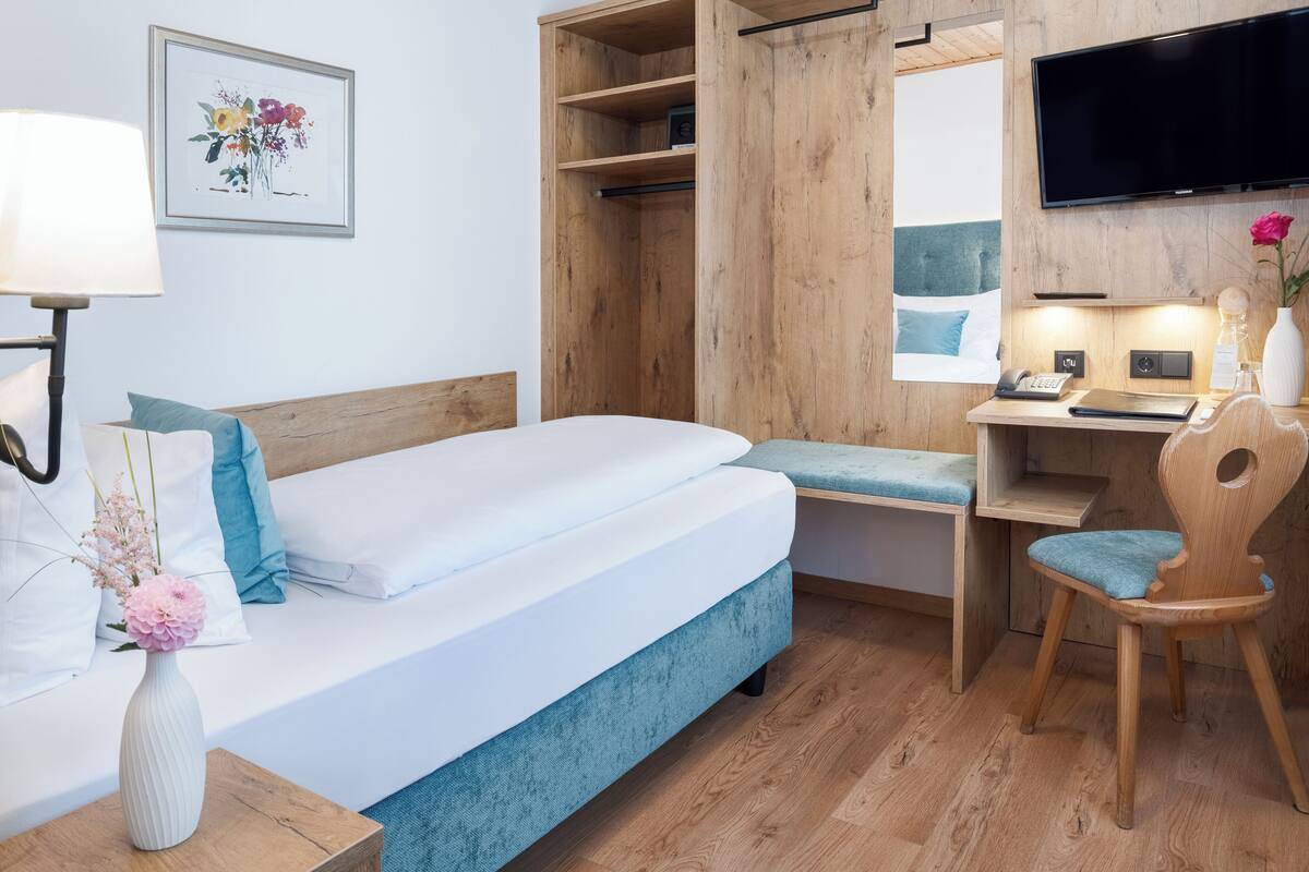 A bedroom with a bed, a desk, a chair, a TV, and a wooden wardrobe.