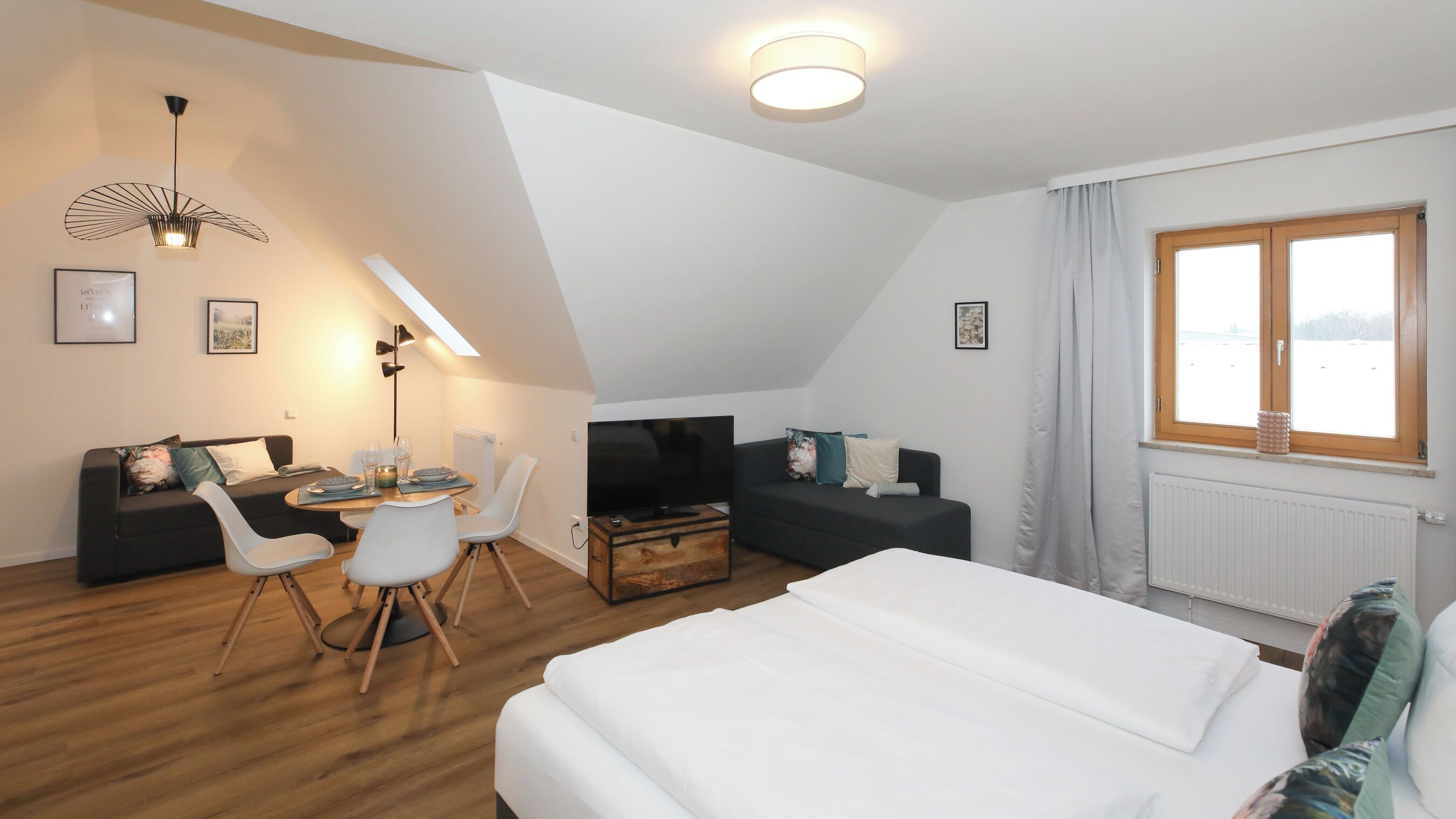 Et moderne hotelværelse med seng, spiseplads, fjernsyn og et vindue med gardiner.