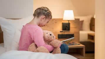 Un niño sentado en una cama con un osito de peluche, leyendo un libro.