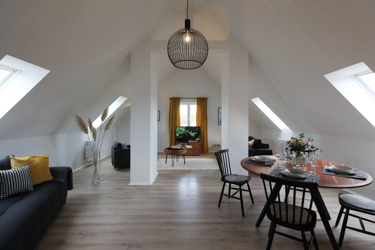 A modern loft apartment with a dining area, a living room, and a view of the outdoors.