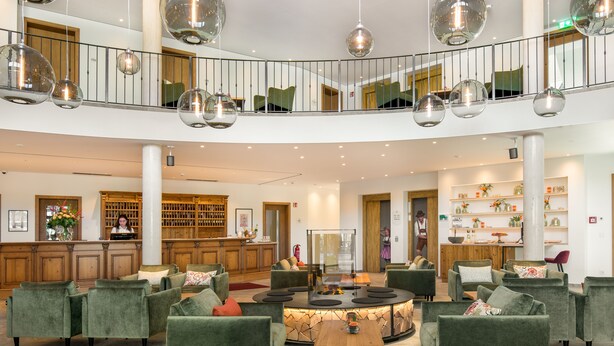 A spacious lobby with a central seating area, a reception desk, and a staircase connecting two floors. - Hotel Obermaier (Munich)
