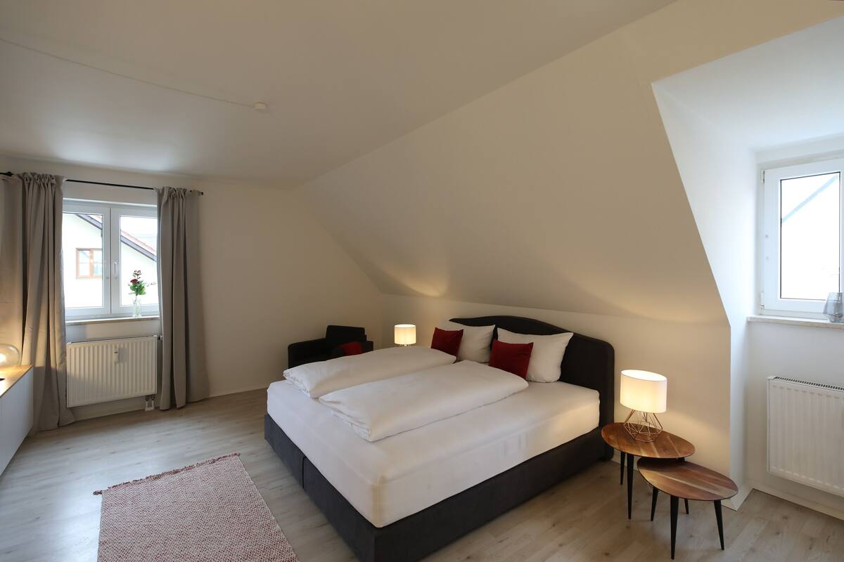 A bedroom with a large bed, bedside tables, a window with curtains, and a radiator.
