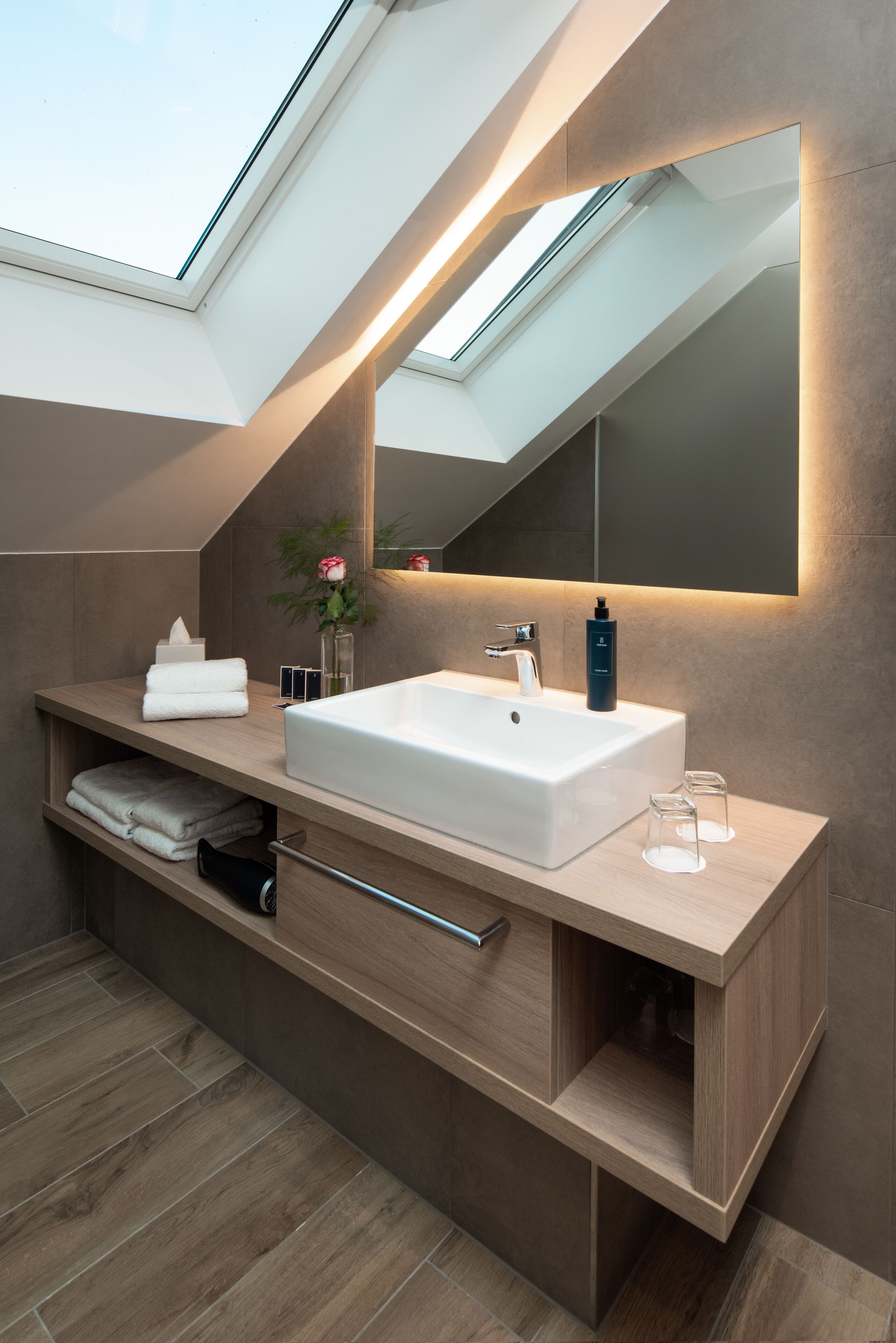 Un baño moderno con tragaluz, un espejo grande, un lavabo blanco y muebles de madera.
