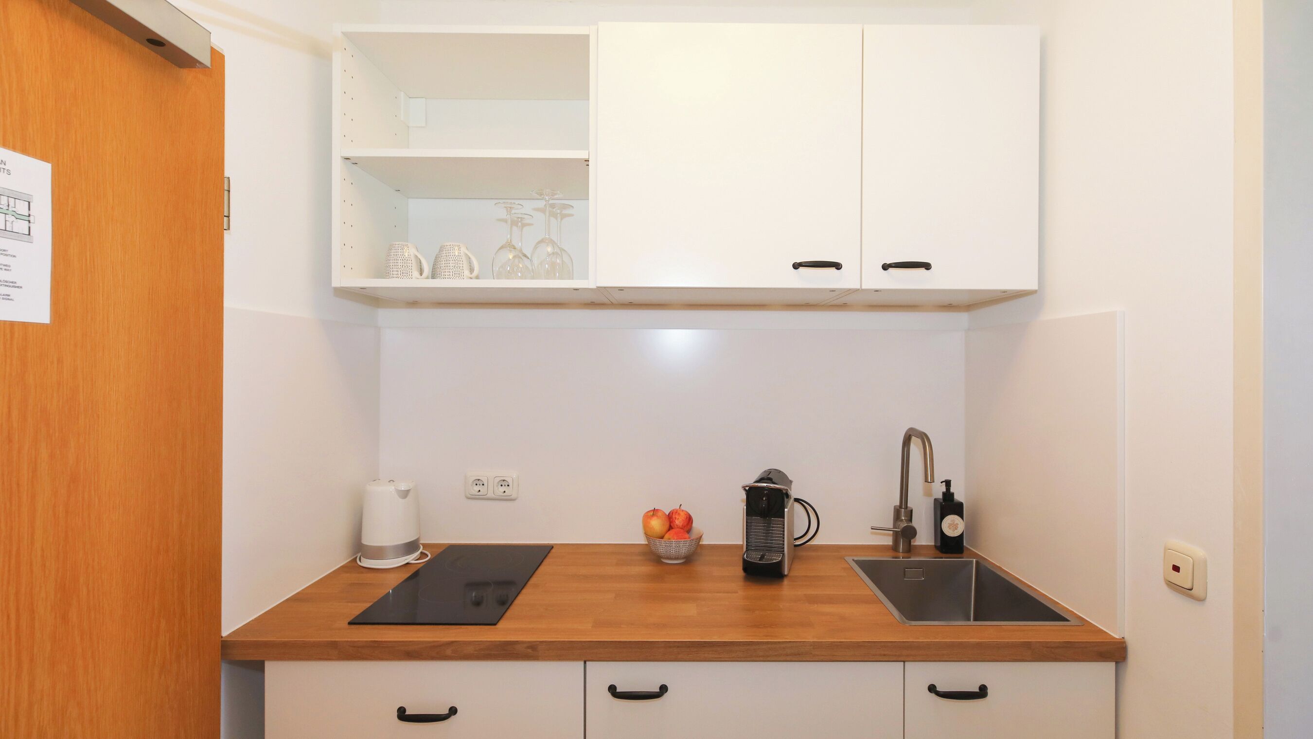 Una cucina compatta con due lavandini, una macchina per il caffè e una ciotola di frutta.